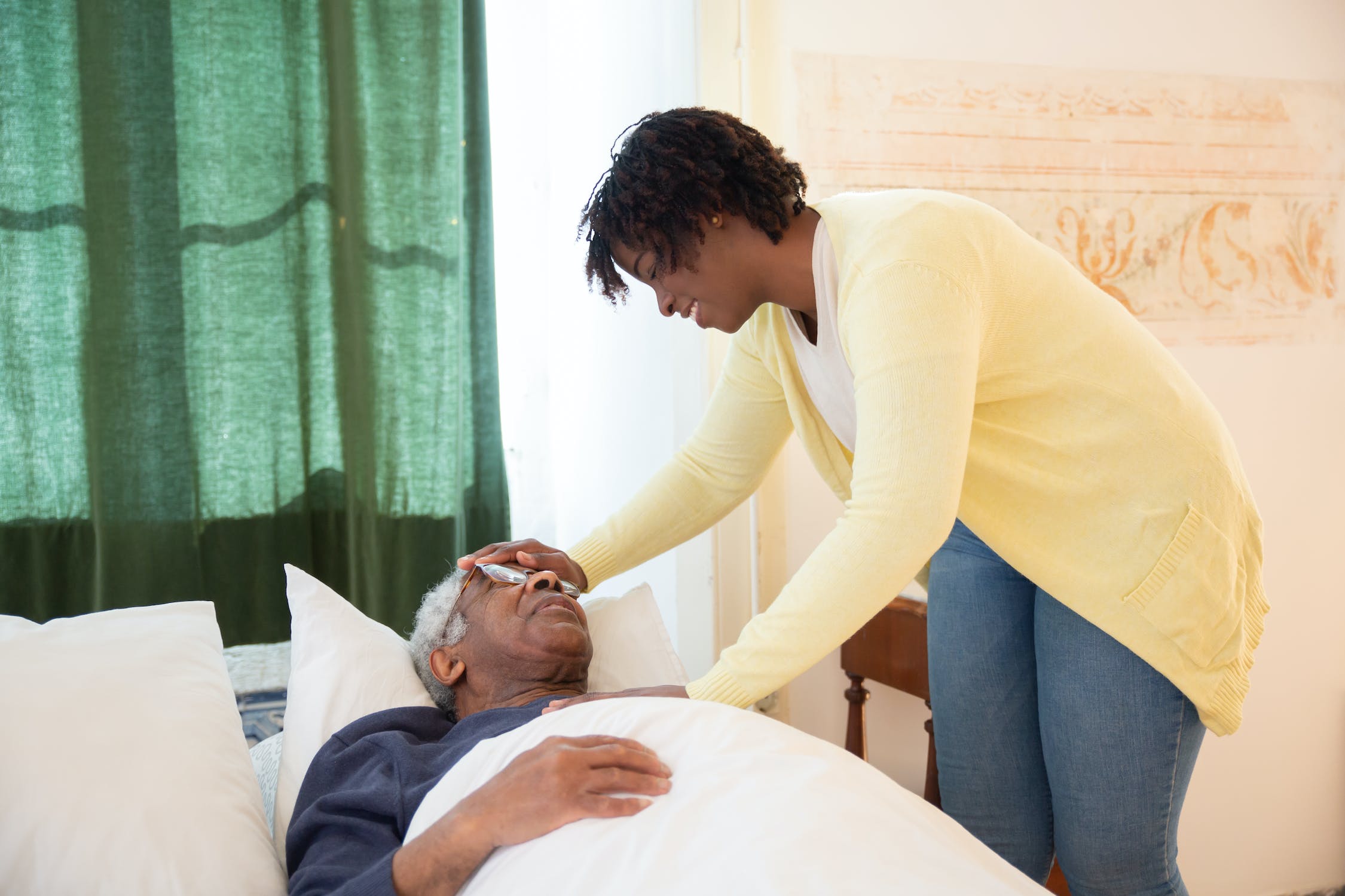 Support worker caring for elderly man in bed